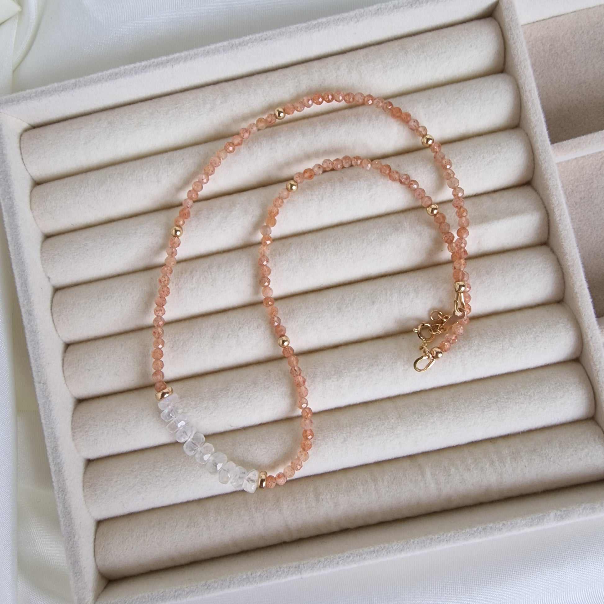 Necklace with pink beads and gold clasp on a beige jewelry box