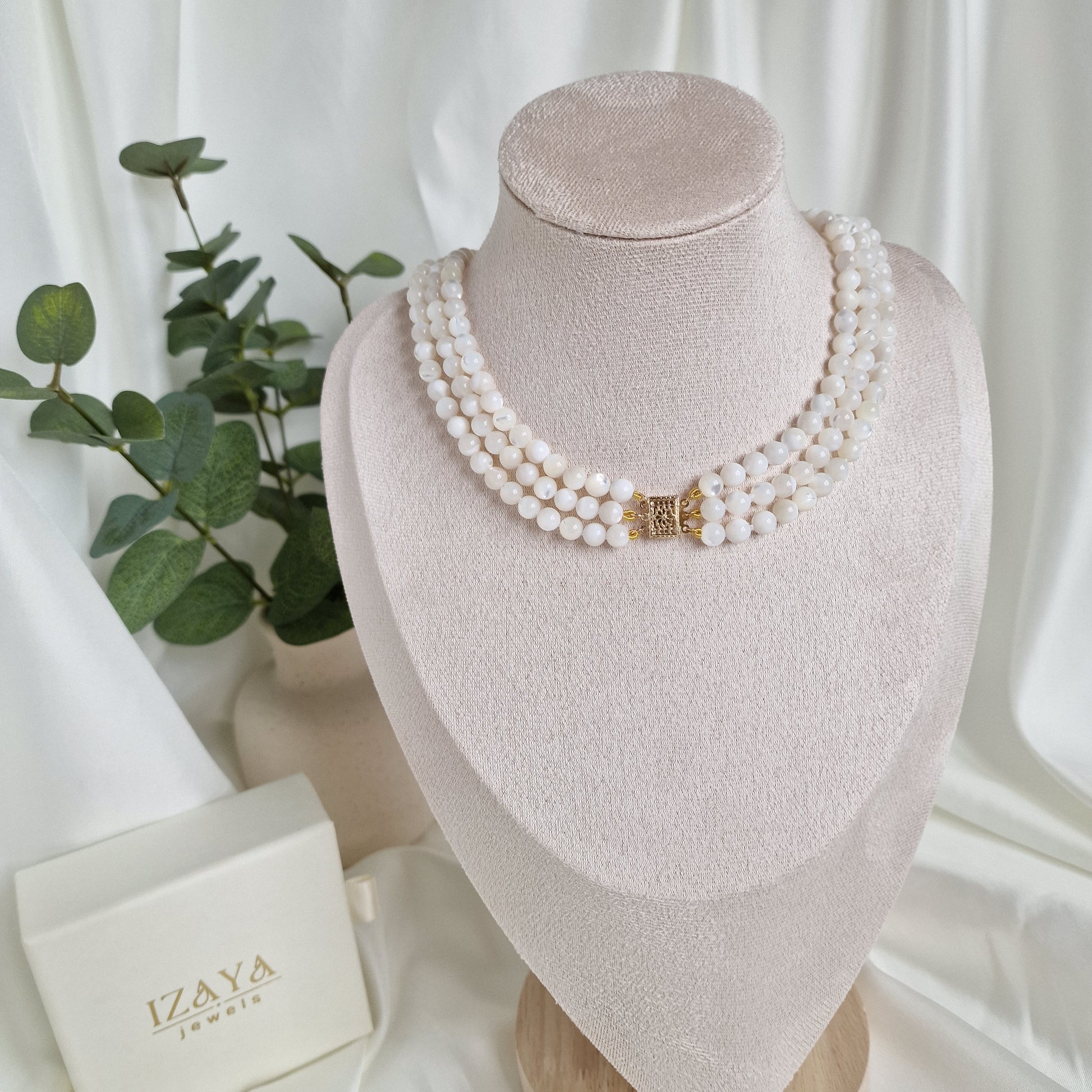 Pearl necklace on a mannequin head with a white box and green leaves in the background