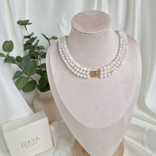 Pearl necklace on a mannequin head with a white box and green leaves in the background